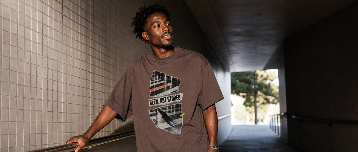 Adult model wearing the 3o1d SEEN, NOT STORED oversized T-shirt in Mocha in a tiled city passage.