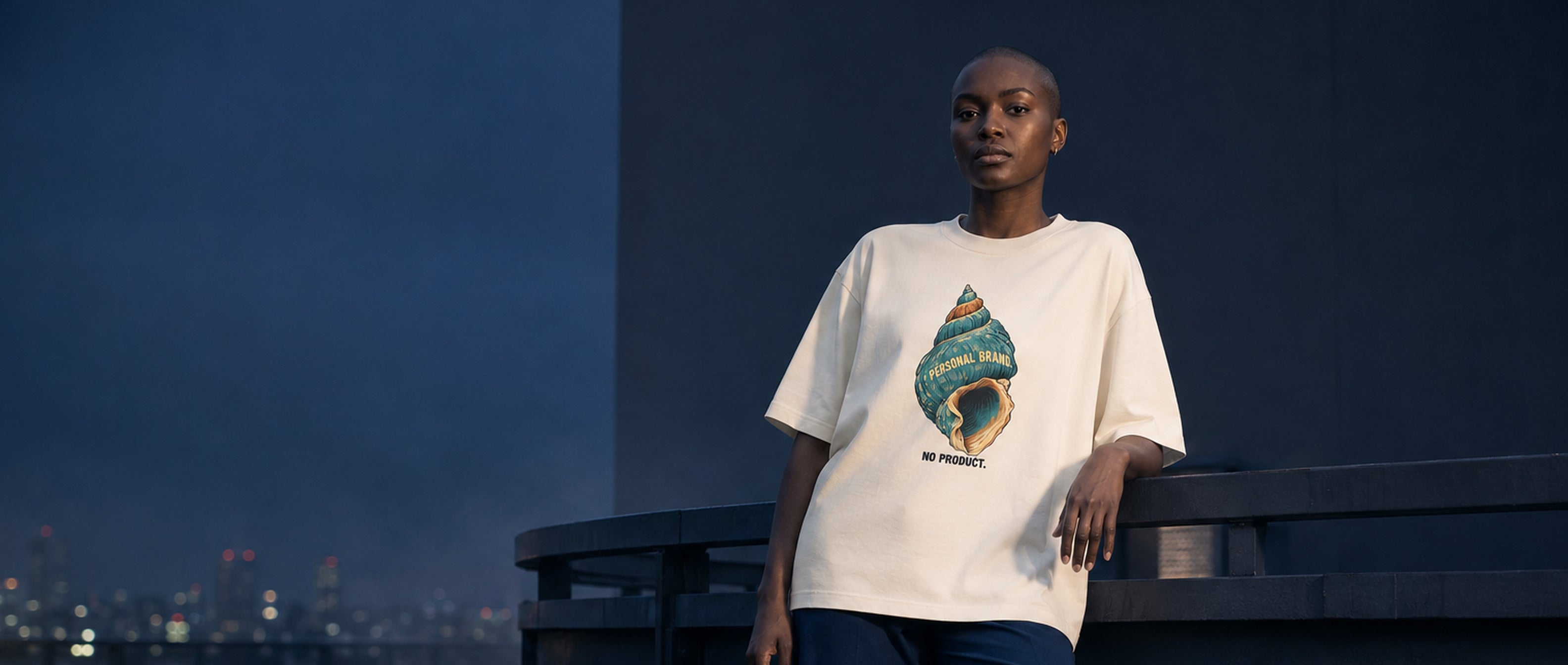 Adult model wearing the 3o1d PERSONAL BRAND. NO PRODUCT. oversized T-shirt in Cream on a blue-hour rooftop.